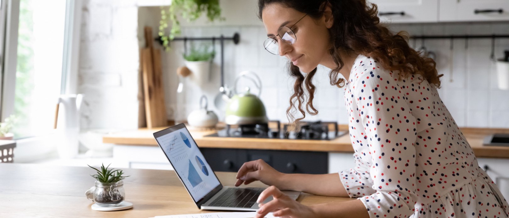 Serious young woman wearing glasses calculating investments on laptop